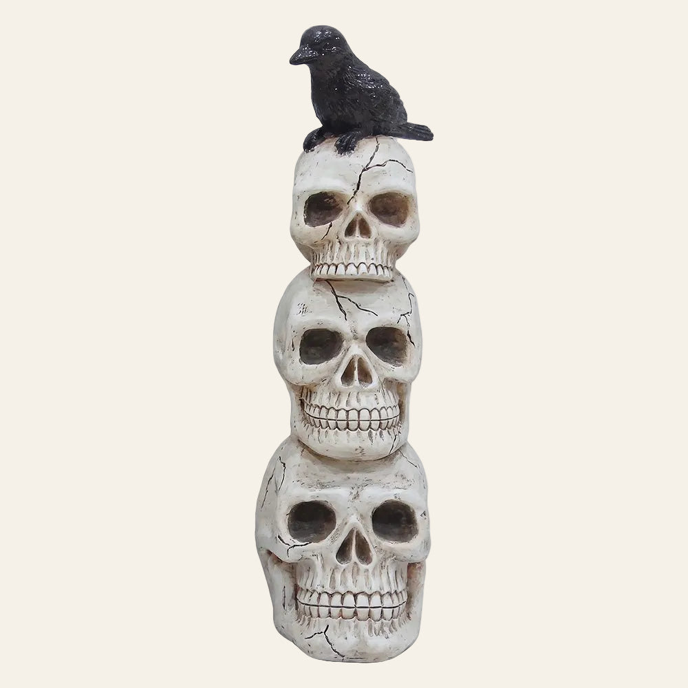 Drie decoratieve schedels uit wit kunststof van groot naar klein boven op elkaar met op de bovenste schedel een zwarte kraai als productfoto