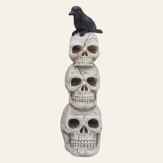 Drie decoratieve schedels uit wit kunststof van groot naar klein boven op elkaar met op de bovenste schedel een zwarte kraai als productfoto