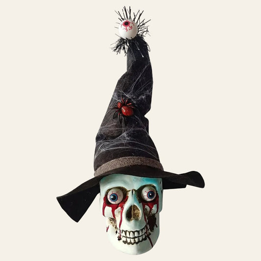 Decoratieve schedel in wit kunststof met een zwarte heksenhoed op met een dikke rode spin en vanboven op de punt van de hoed hangt een oog voor halloween als productiefoto
