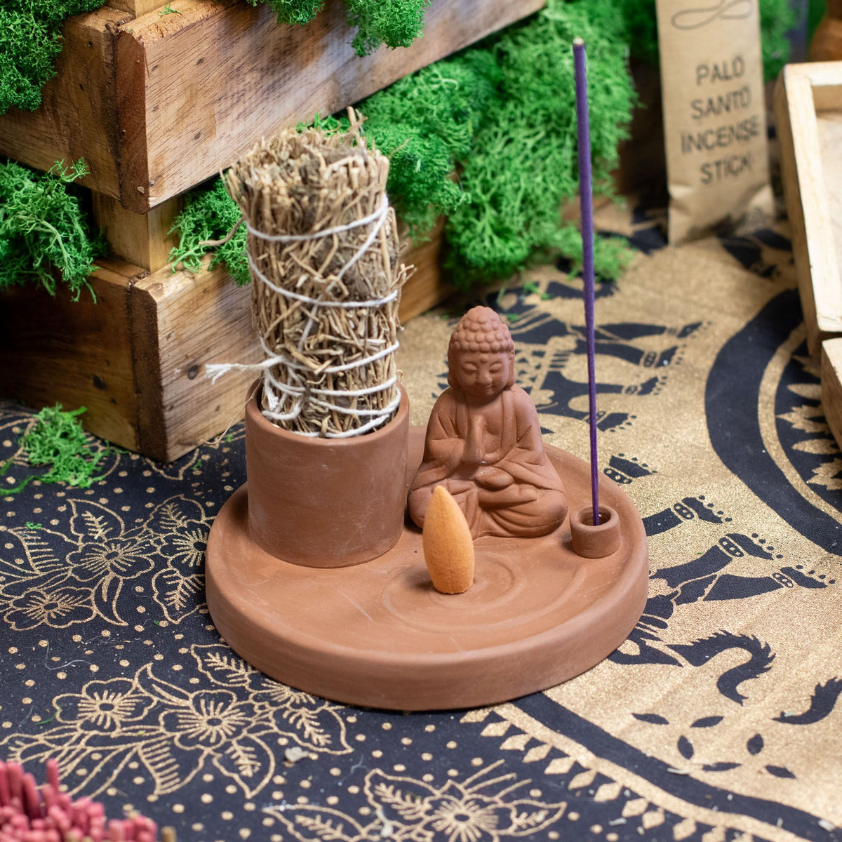 Terracotta Boeddha wierookhouder voor stokjes en kegels op een tafel met smudgestick, wierookstokje en een wierookkegel als detailfoto