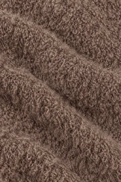 Detail van de bouclé stofstructuur van damestrui met decoratieve stiksels.