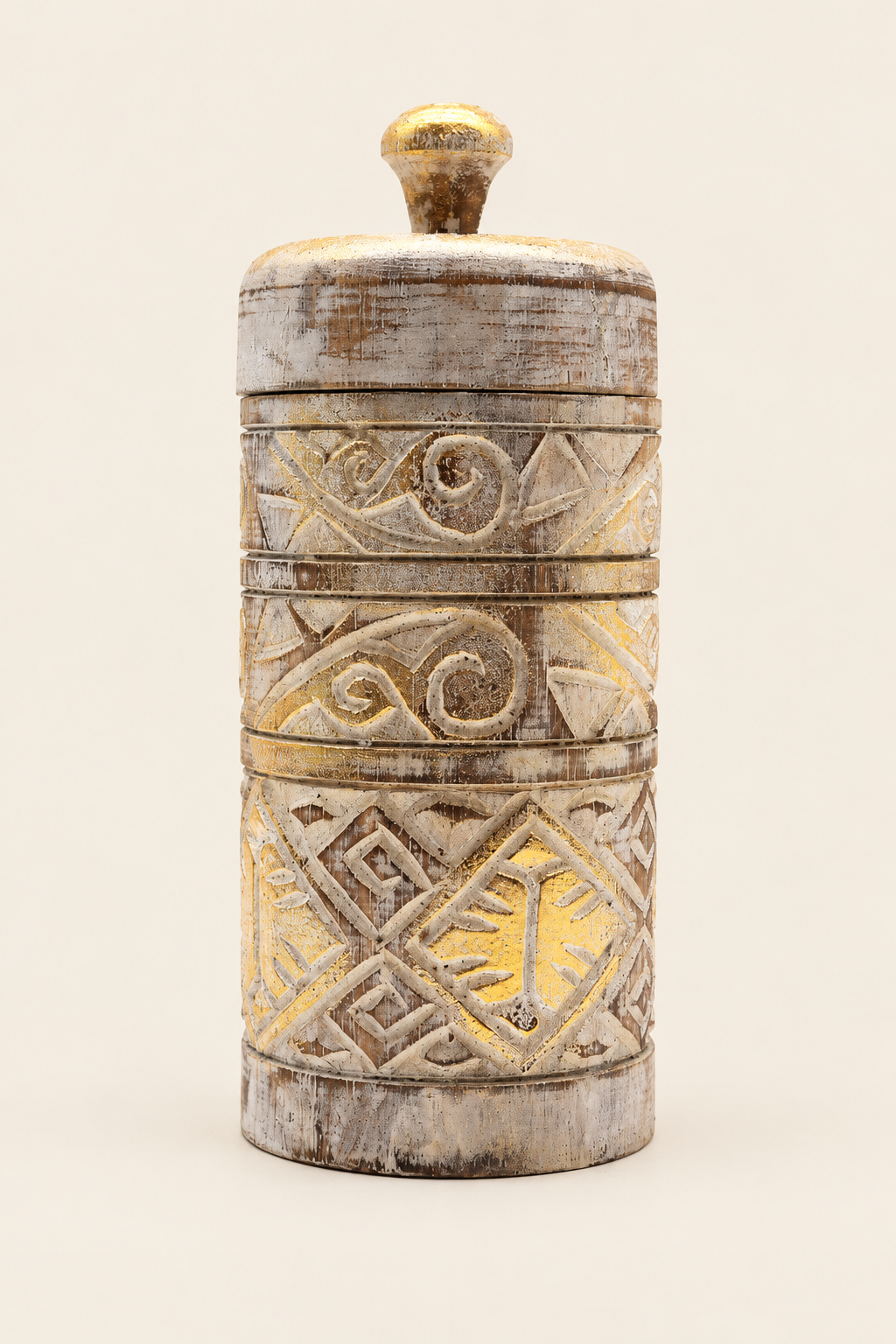 Cilindervormige houten opbergpot met deksel, verweerd witte afwerking, gouden accenten en uitgesneden geometrische patronen op een lichtbeige achtergrond.