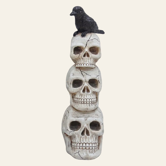 Drie decoratieve schedels uit wit kunststof van groot naar klein boven op elkaar met op de bovenste schedel een zwarte kraai als productfoto