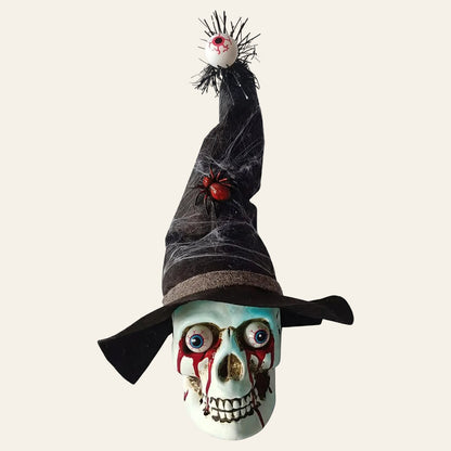Decoratieve schedel in wit kunststof met een zwarte heksenhoed op met een dikke rode spin en vanboven op de punt van de hoed hangt een oog voor halloween als productiefoto