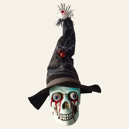 Decoratieve schedel in wit kunststof met een zwarte heksenhoed op met een dikke rode spin en vanboven op de punt van de hoed hangt een oog voor halloween als productiefoto