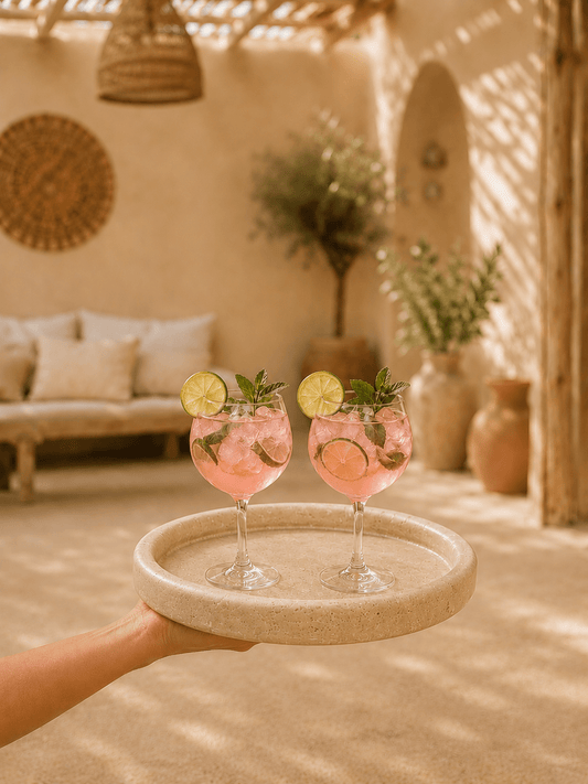 Dienblad van travertijn met opkant gevuld met 2 heelijk roze cocktails op een gezellig terras in geblurd dieptezicht