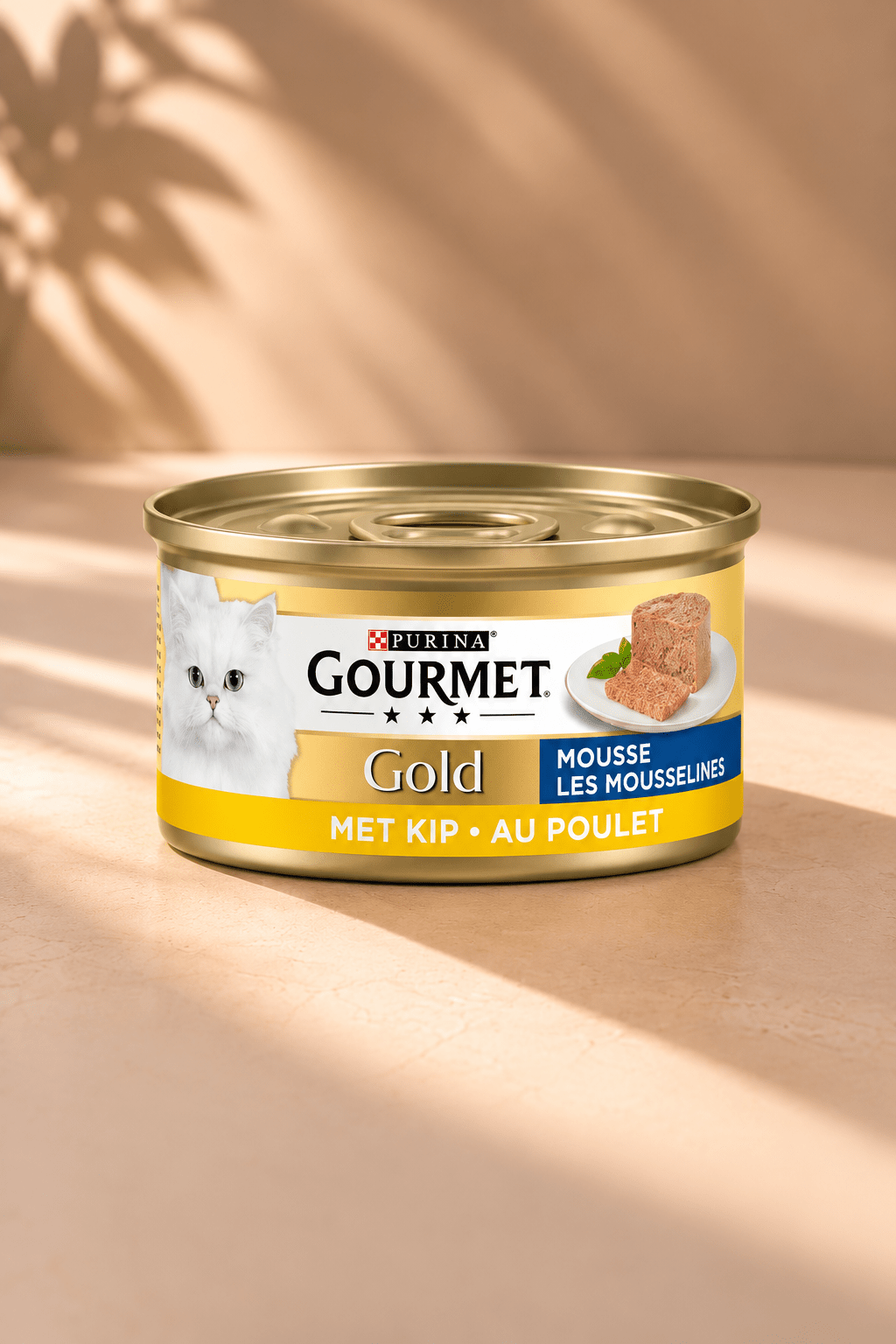 Gourmet Gold fijne mousse met kip, goudgeel kattenvoerblik van 85 gram met witte kat op beige achtergrond met bladschaduw.