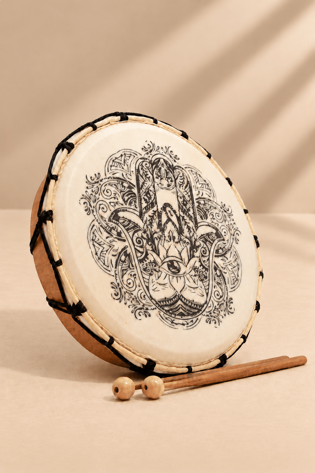 Hamsa sjamanistische trommel met gedetailleerd handmotief en twee houten kloppers op een lichtbeige achtergrond