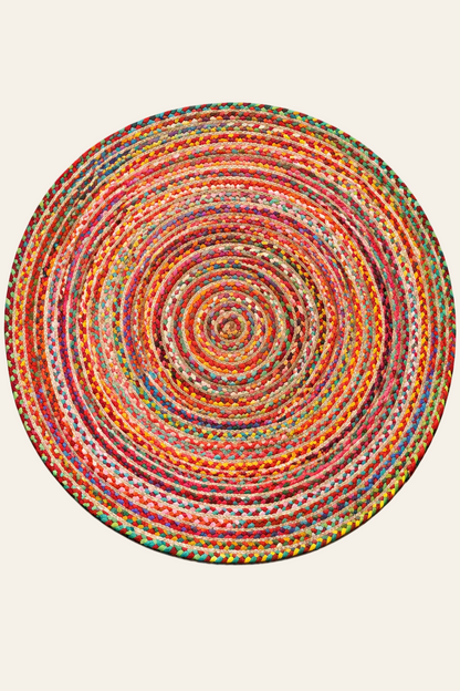 Handgemaakt rond vloerkleed in multicolor met concentrische vlechtstructuur van jute en gerecycleerde textielmaterialen op een neutrale lichte achtergrond.