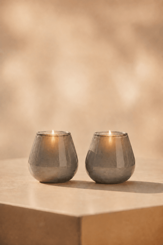 Ivory waxinelichthouder in mat grijze tint oplichtend op een lichteige tafel met geblurde achtergrond