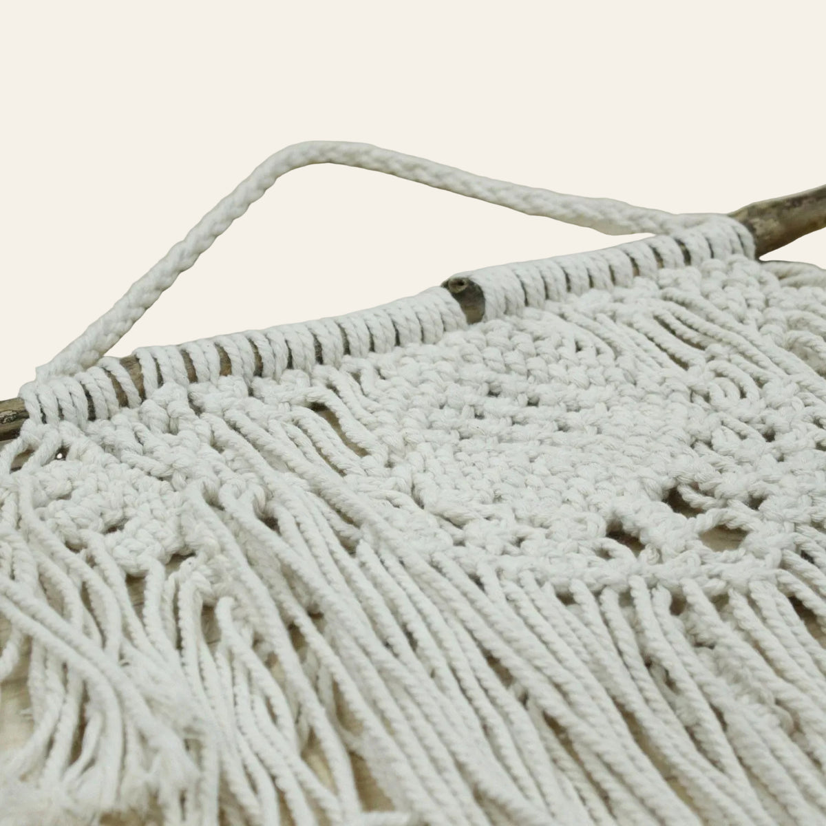 Naturel macramé wanddecoratie met houten ophangtak, gevlochten patronen en lange franjes detailfoto