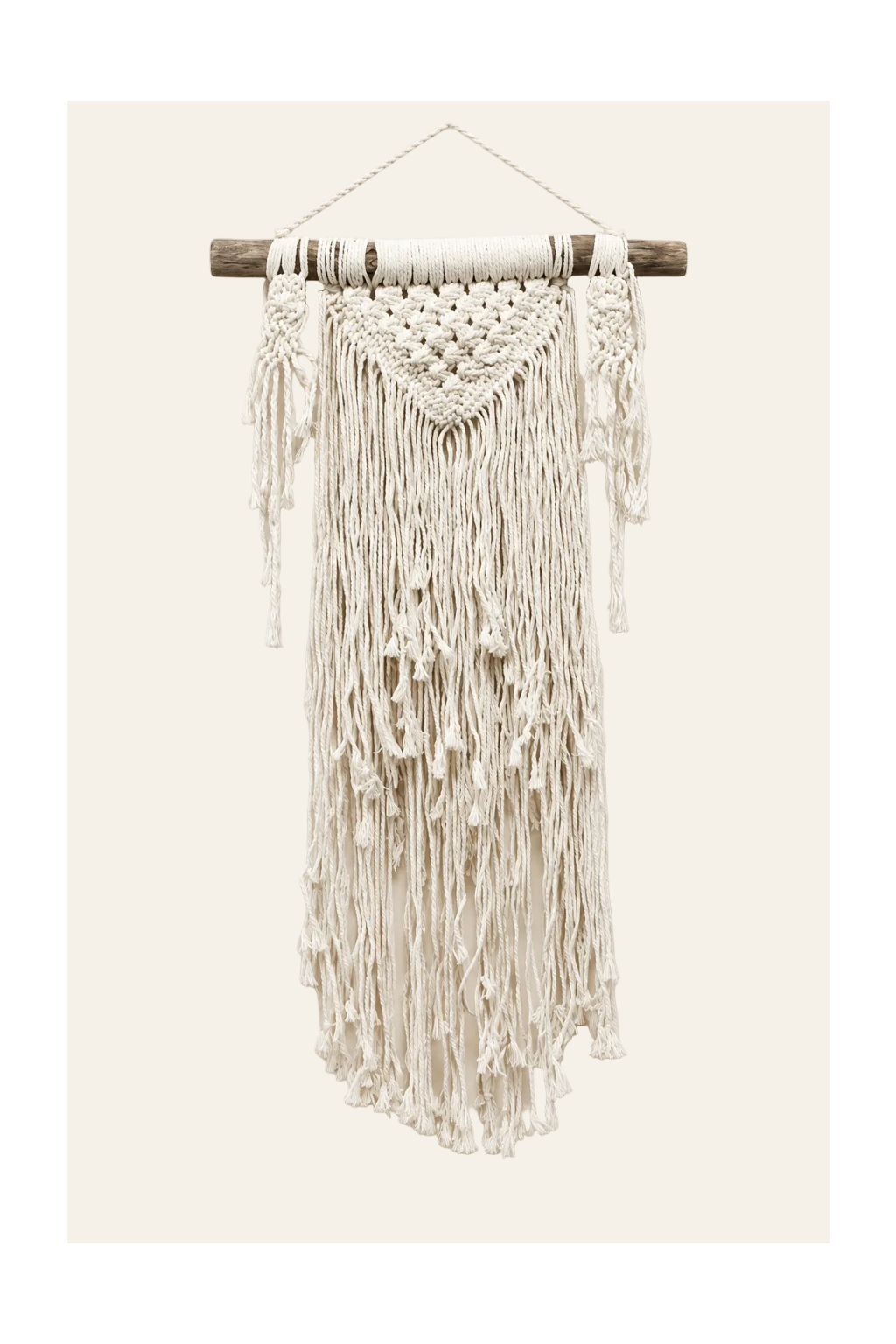 Handgemaakte crèmekleurige macramé wanddecoratie Natuurlijke overvloed met houten ophangtak, verfijnde knooppatronen en lange franjes op een lichtbeige achtergrond.