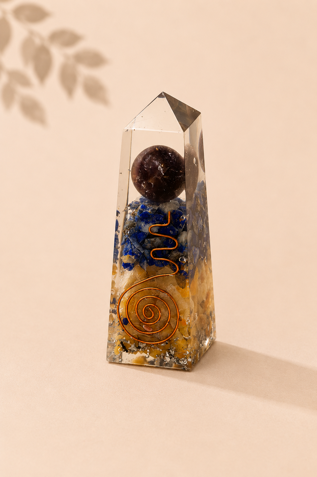 Orgoniet obelisk met lapis lazuli en gele aventurijn op een beige gebladerde achtergrond