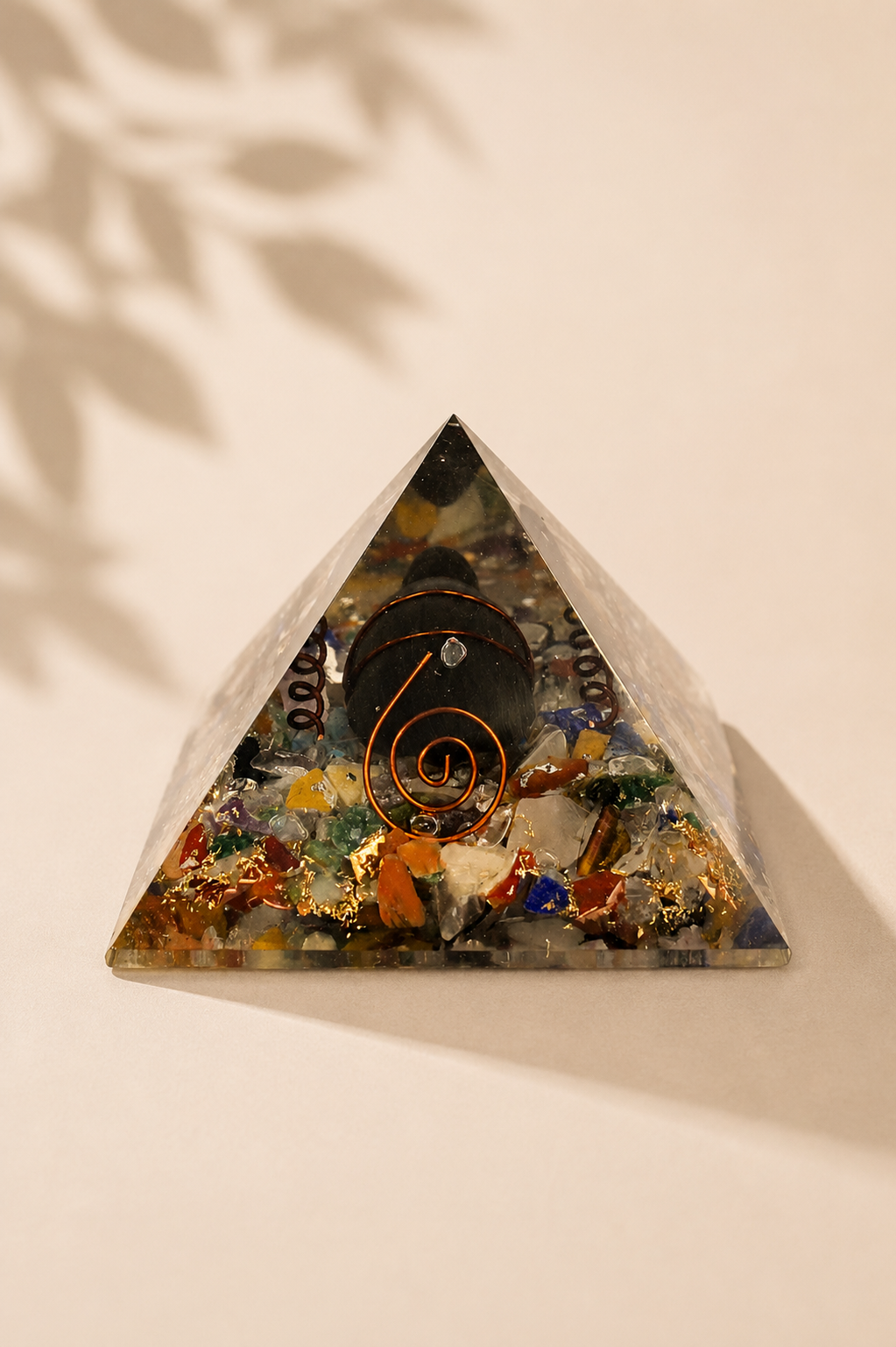 Orgoniet piramide 60 mm met edelsteenchips, koper en schildpad op een gebladerde beige achtergrond