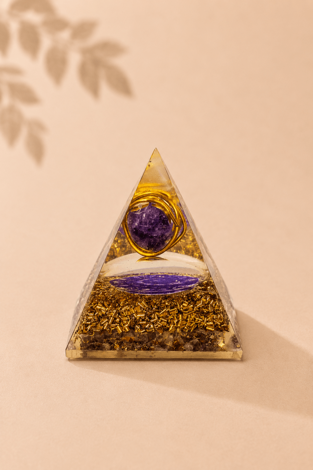Orgoniet piramide met amethist en koperspiraal op een beige gebladerde achtergrond