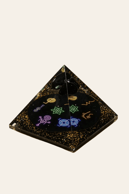 Orgoniet piramide met zwarte obsidiaan en chakra-symbolen op een lichte beige achtergrond als product foto