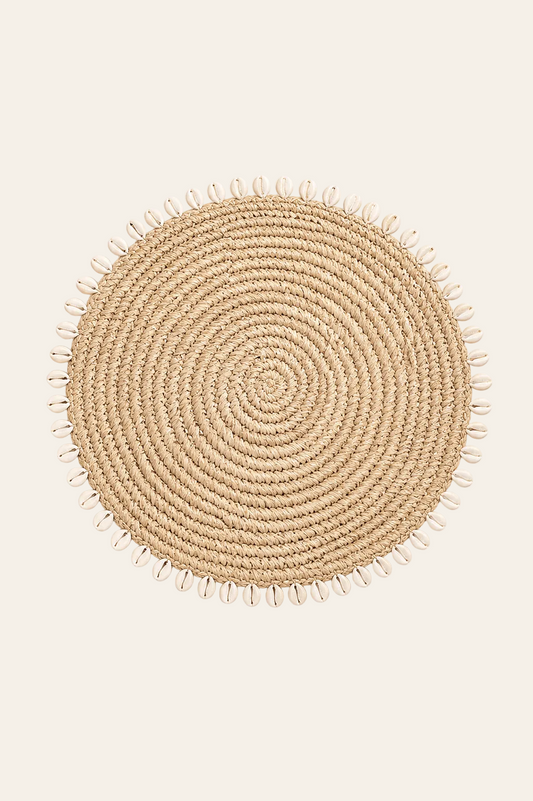 Ronde raffia pannenonderzetter met kaurischelpen op een licht beige achtergrond