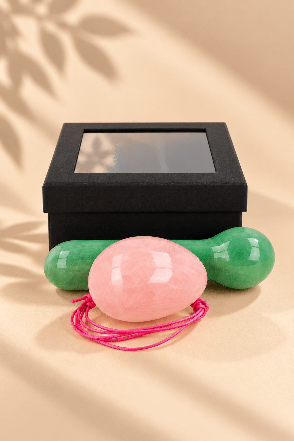 Yoni massageset met roze rozenkwarts ei, groene aventurijn massagestaaf en zwart geschenkdoosje op beige achtergrond.