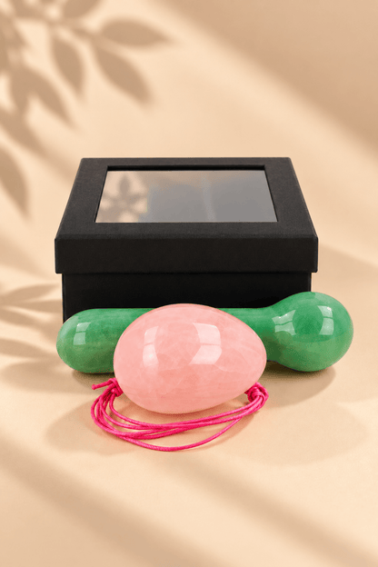 Yoni massageset met roze rozenkwarts ei, groene aventurijn massagestaaf en zwart geschenkdoosje op beige achtergrond.