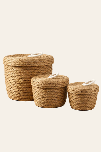 Set van 3 ronde gevlochten opbergmanden van naturel zeegras met bijpassende deksels en witte katoenen lushandvatten op lichtbeige achtergrond