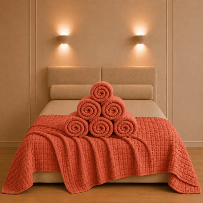 Swami bedsprei in terracottaroodkleur op een tweepersoonsbed met decoratief opgerolde stof en een verzorgde boutique presentatie