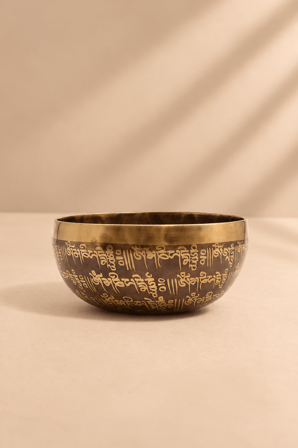 Tibetaanse genezingskom van 16 cm met goudkleurige mantra gravures en warme bronskleur op een lichtbeige achtergrond
