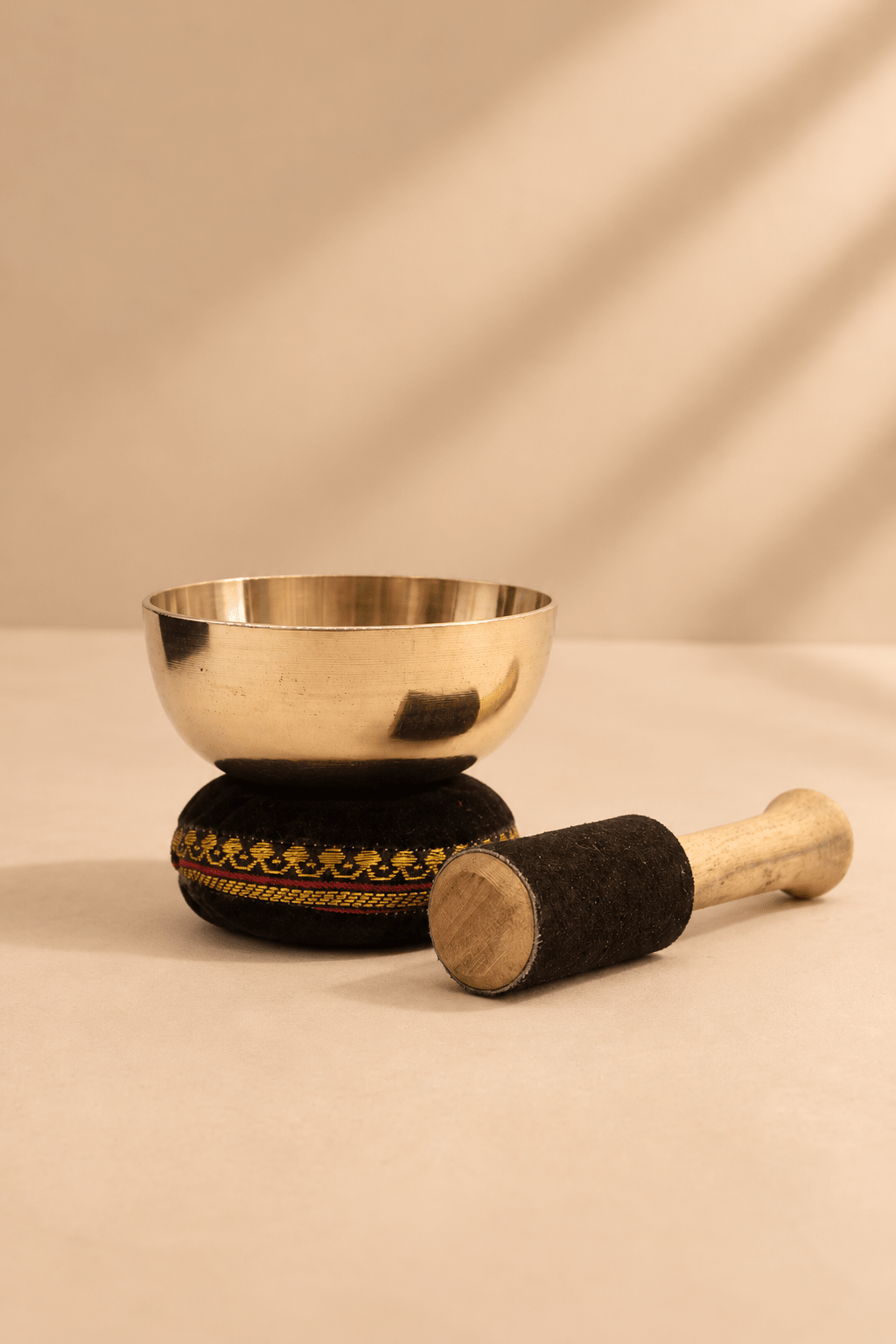Tibetaanse klankschaal 9 cm uit Nepal op zwart sierkussen met houten klopper in een warme beige omgeving