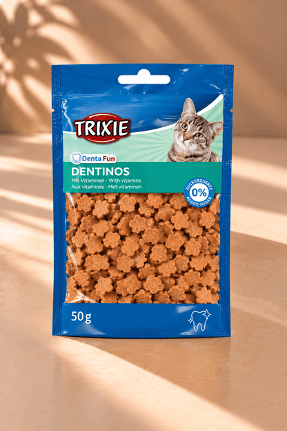 Trixie Denta Fun Dentinos kattensnacks met vitaminen, blauwe verpakking van 50 gram met kleine bruine hapjes op beige achtergrond.