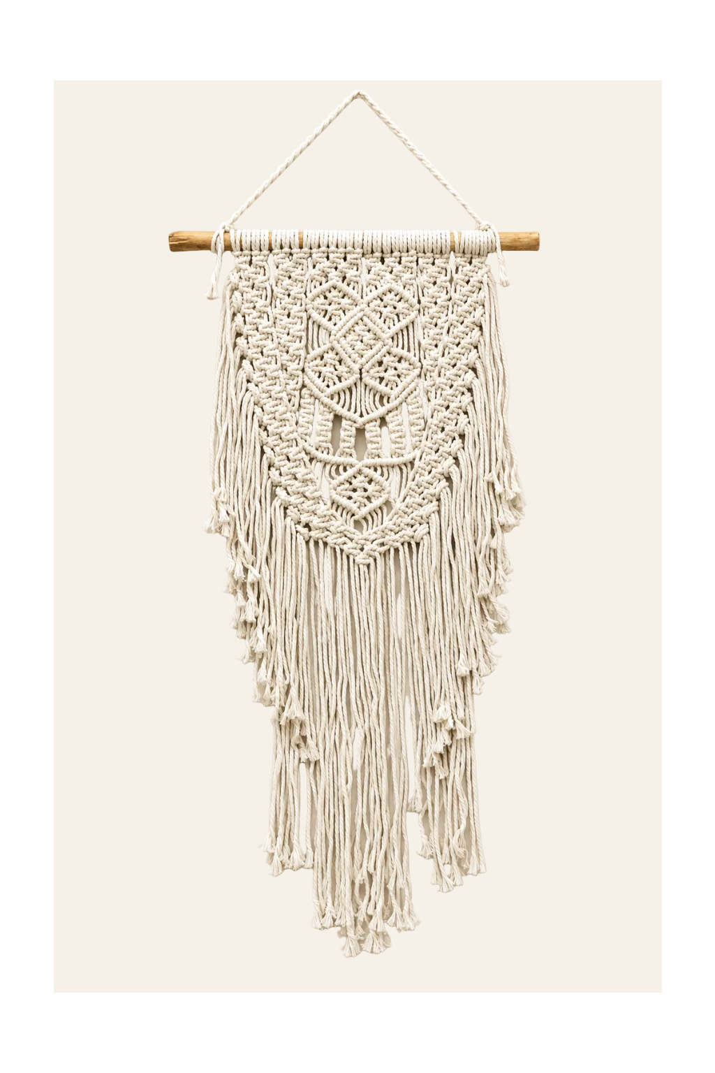 Handgemaakte macramé wanddecoratie Abundance in naturel met geometrische knooppatronen, houten ophangtak en lange franjes op een lichtbeige achtergrond.