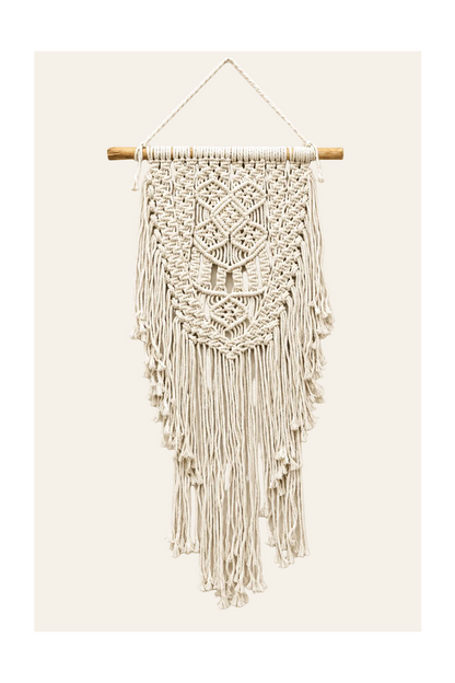 Handgemaakte macramé wanddecoratie Abundance in naturel met geometrische knooppatronen, houten ophangtak en lange franjes op een lichtbeige achtergrond.