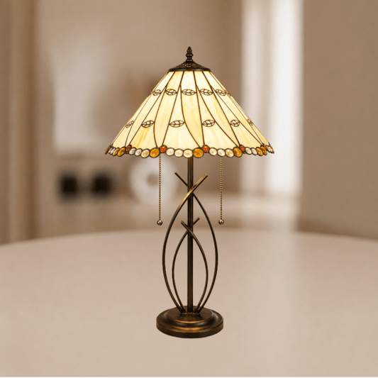 Brandende Tiffany tafellamp met beigekleurige glas-in-loodkap en warm licht boven metalen onderstel