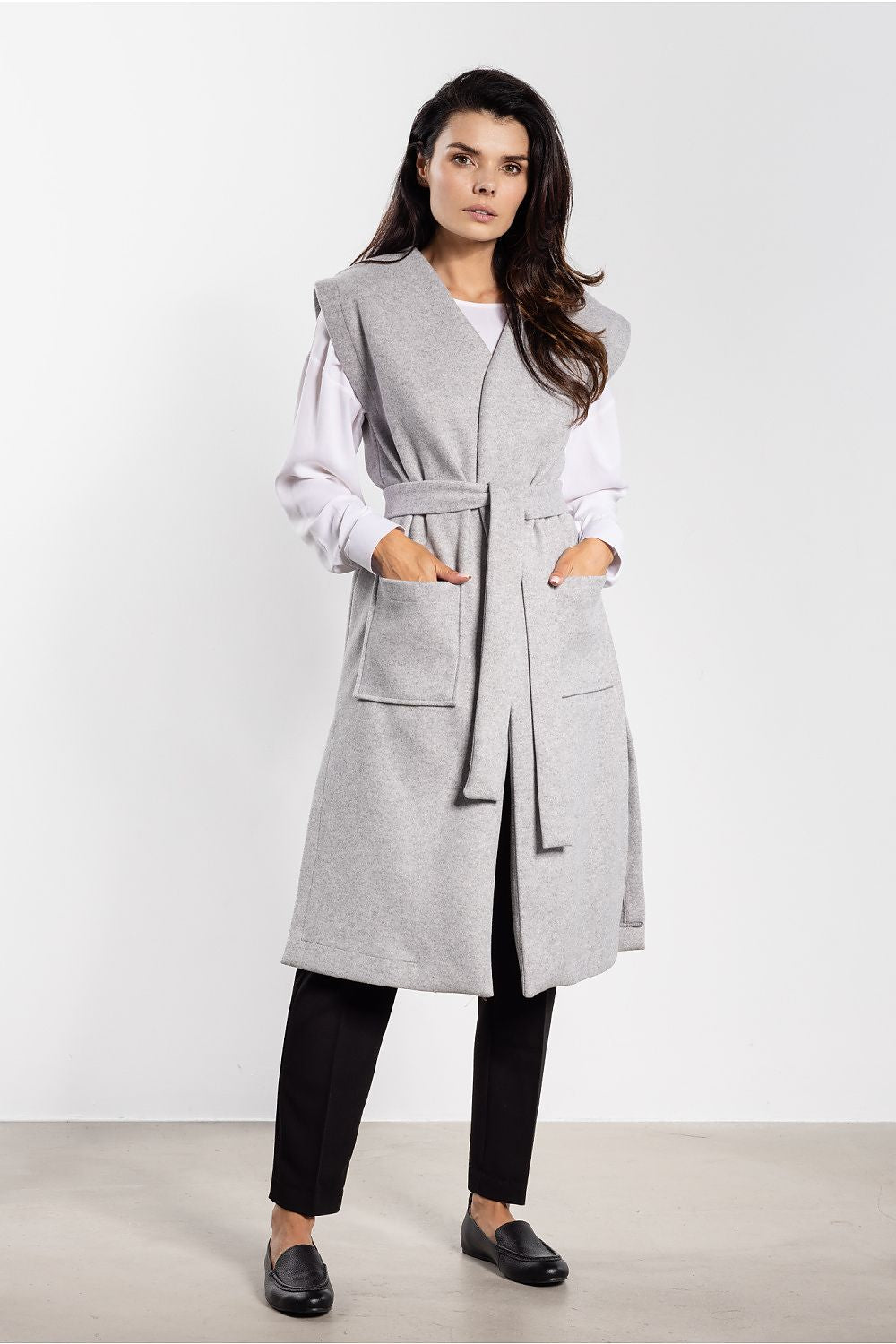 Voorkant van een lang grijs mouwloos gilet met ceintuur en twee grote opgestikte zakken.