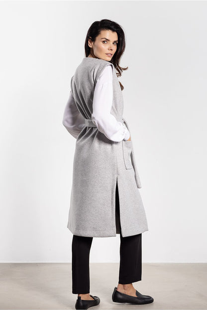 Achterkant van het lange grijze gilet met ceintuur en diepe zijsplit op een staand model.