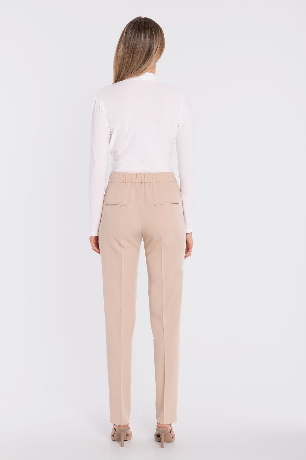 Achterkant van de beige pantalon brengt de gladde achterkant en rechte pijpen duidelijk in beeld op een staand model.