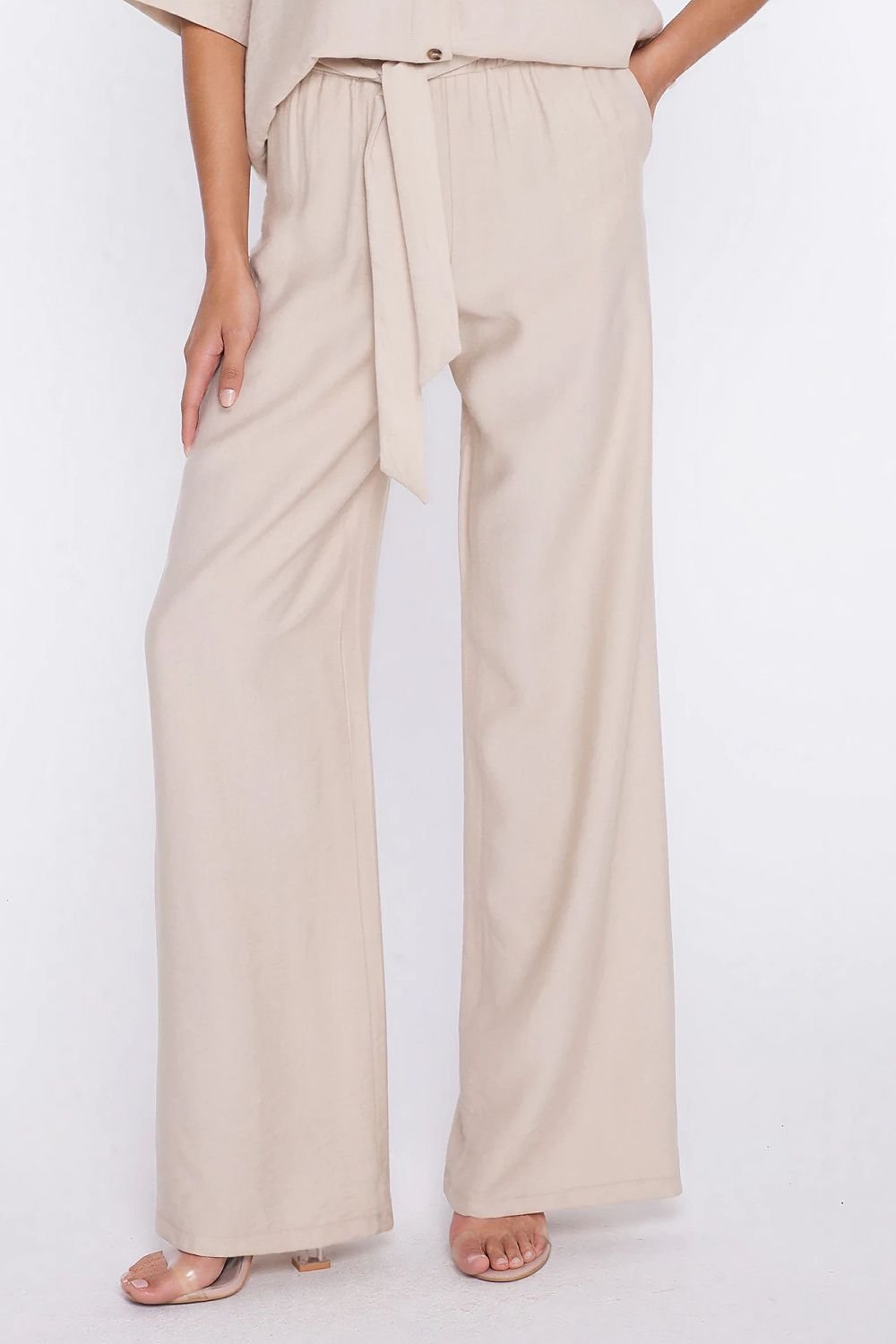 Detail van de lichtbeige pantalon brengt de brede strikriem rond de taille nadrukkelijk in beeld op het model.