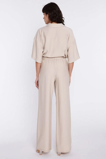 Achterkant van de lichtbeige pantalon brengt de hoge taille en wijde pijpen aan de rugzijde duidelijk in beeld.